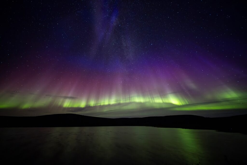 Colourful northern lights with starlit sky and lake reflections