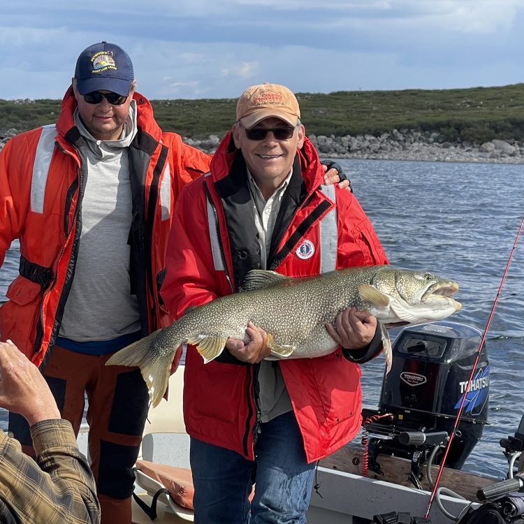 Two friends wearing Mustang Life Jackets, in a boat one man cradling a trophy lake trout