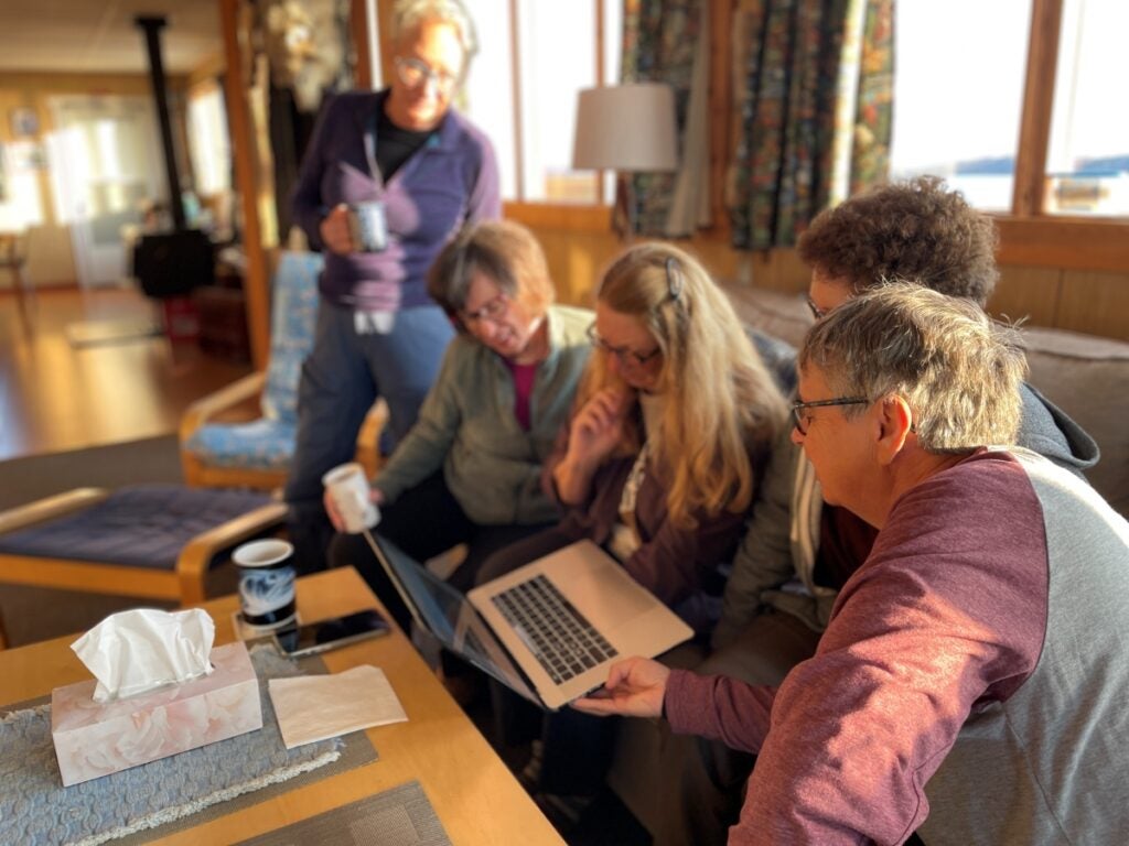 People with coffee in hand, in a lodge with natural light gathered around a computer looking at photos