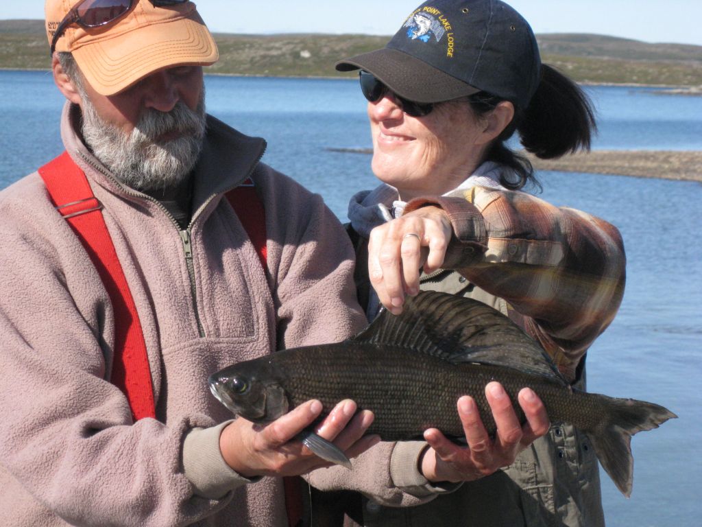 A fishing guide with a very happy guest smiling while holding the dorsal fin of an Arctic Grayling