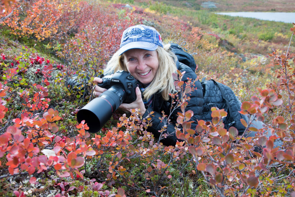 Woman with Canon Camera laying on the tundra smiling taking posed to take a photo.