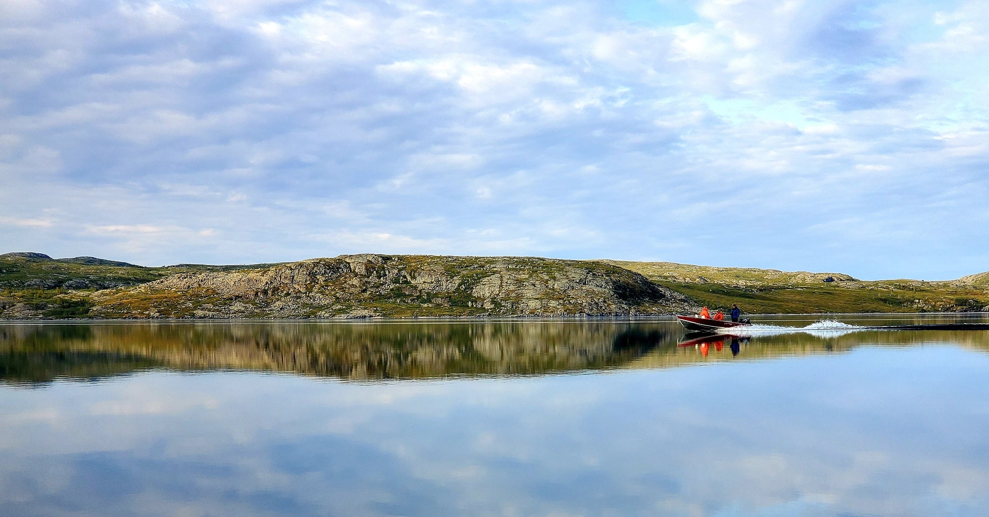 Perfect reflection of land on water with boat moving across the lake