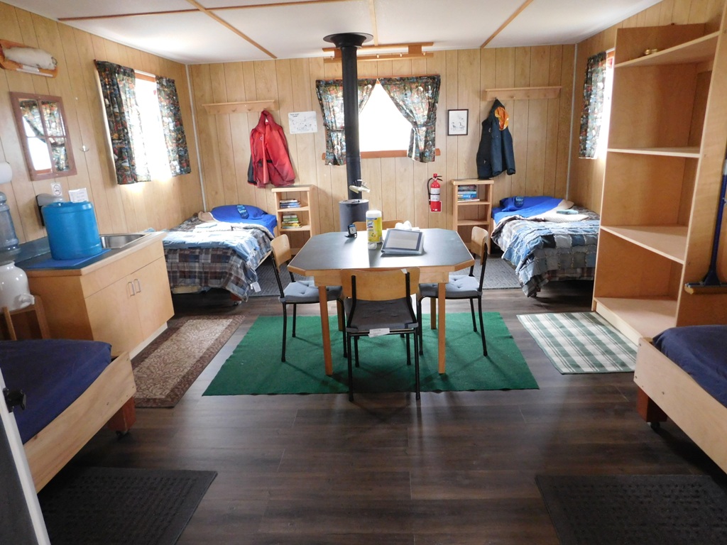 Inside Cabin, 4 Twin Beds with bedding, table and chairs in center of room