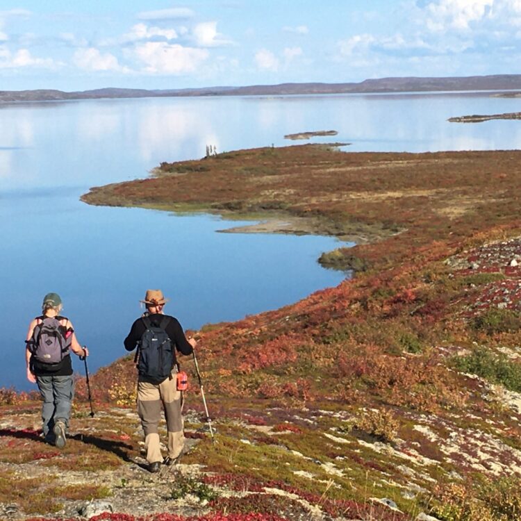 Two people hiking on an esker in Canada's Arctic Tundra overlooking a beautiful lake