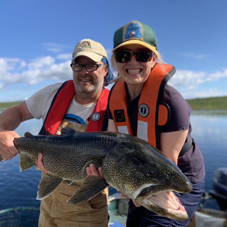 Two people in a boat wearing Mustang Inflatable Lifejackets holding a trophy lake trout