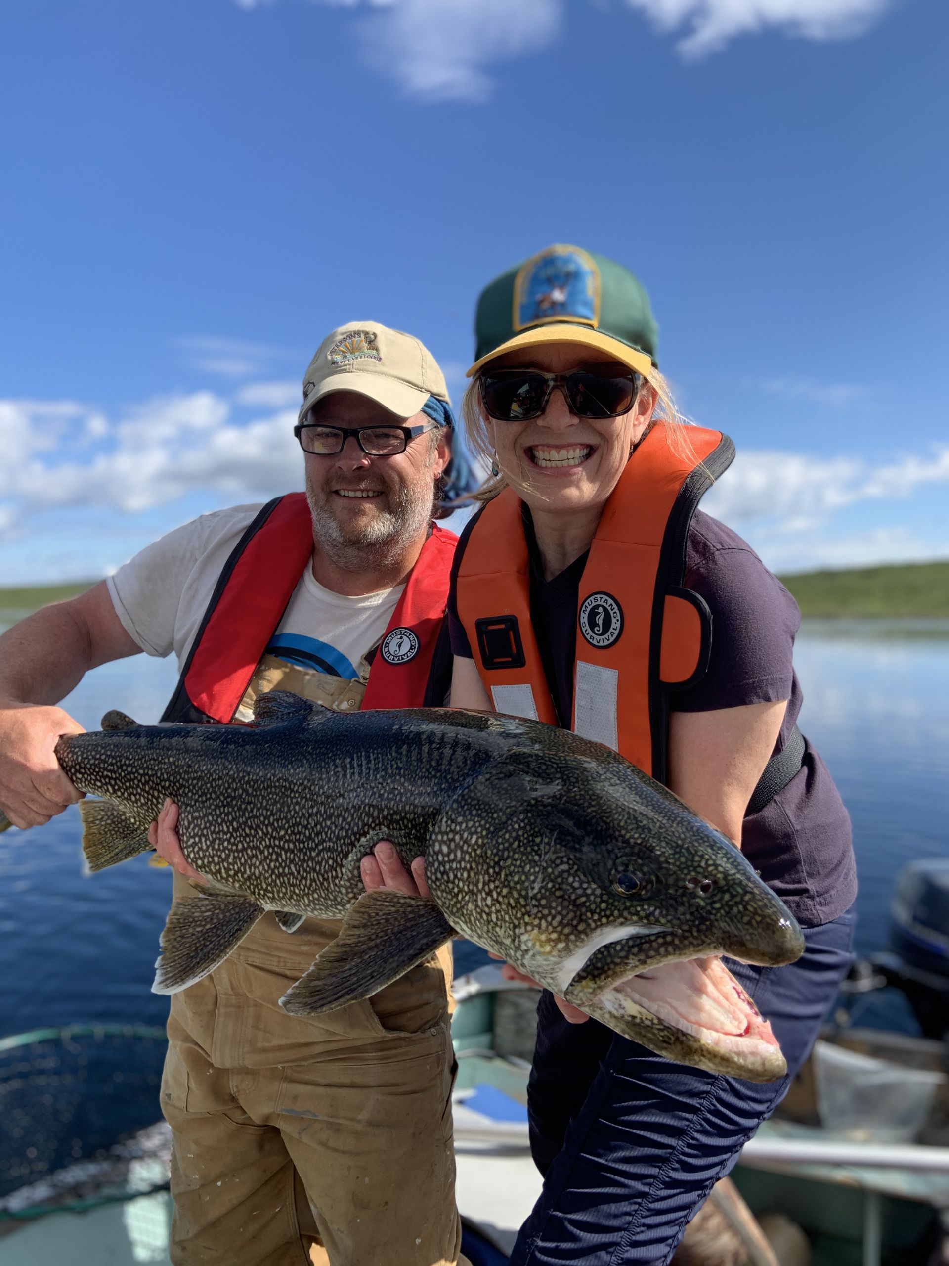 Two people in a boat wearing Mustang Inflatable Lifejackets holding a trophy lake trout