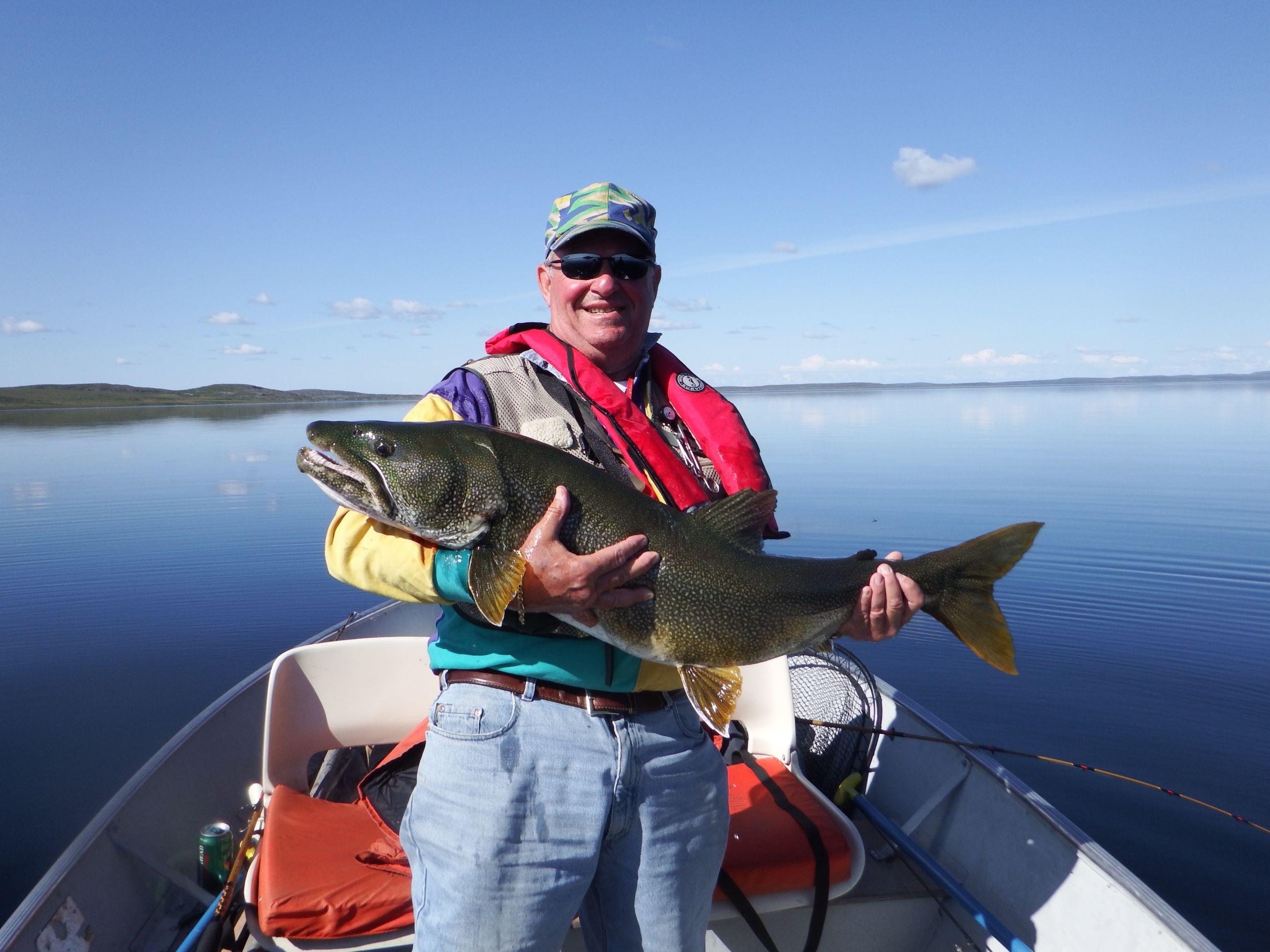 Man wearing inflatable life jacket holding a trophy lake trout in a boat on a lake