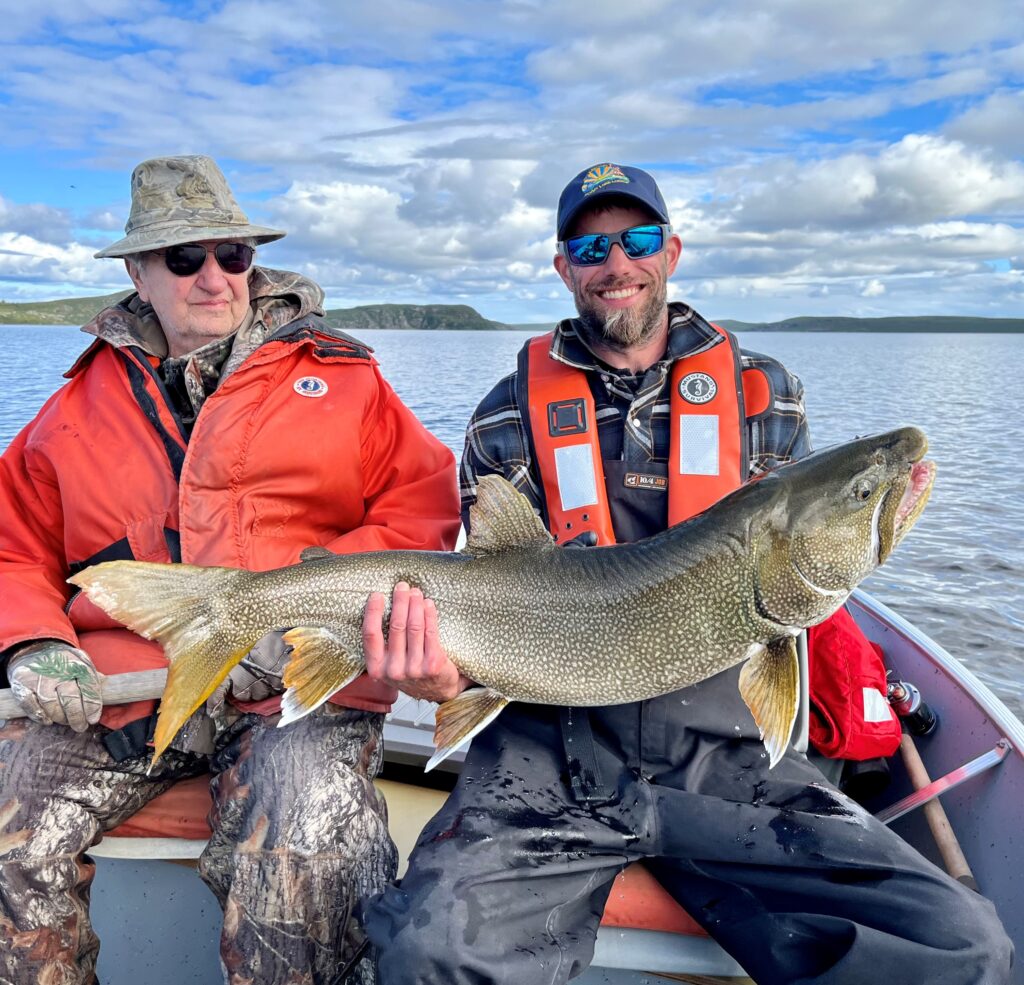 Multi-generations, two men in a boat, one holding a trophy lake trout