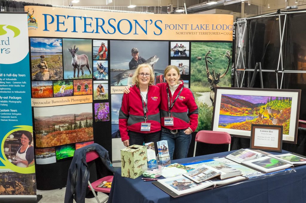 Two women in front of a booth promoting fishing and photography trips