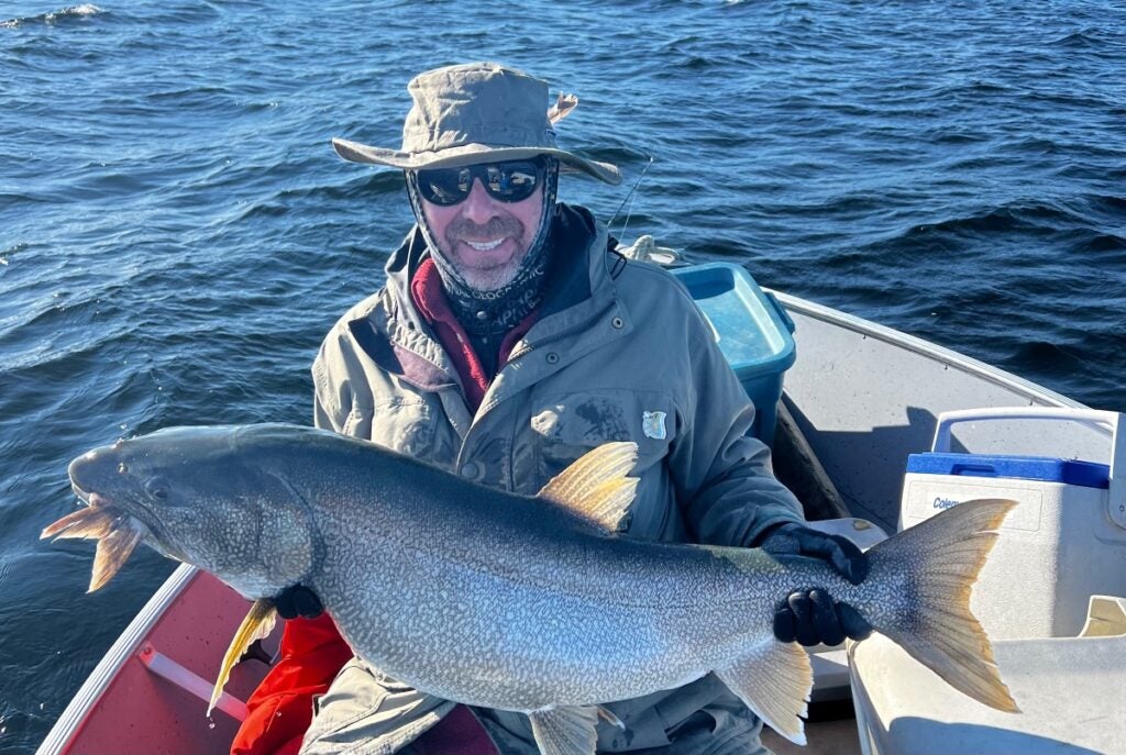 Man holding monster lake trout, the fish as a fin sticking out of it's mouth