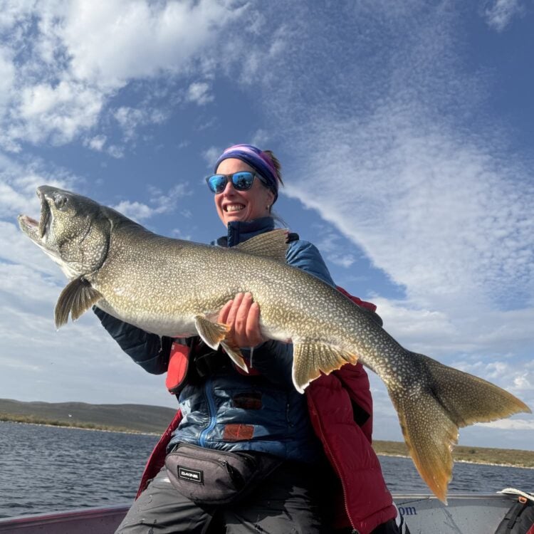 Woman angler holding a massive trophy lake trout on a boat during an NWT fishing lodge trip to Peterson's Point Lake Lodge, in Canada