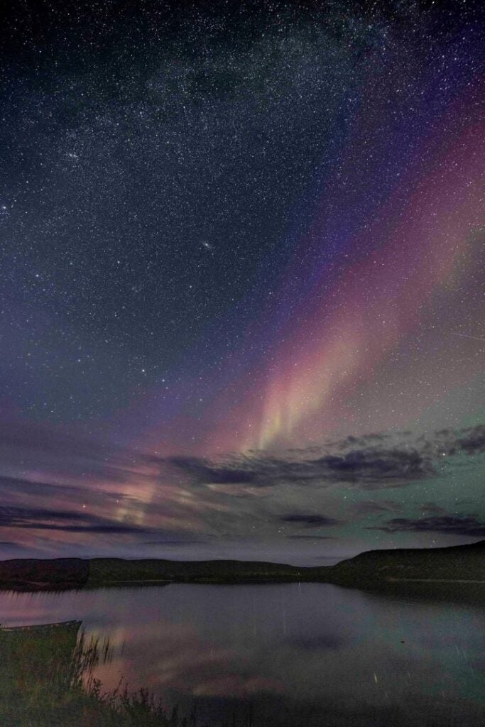 Northern Lights in the night sky and reflected in calm water