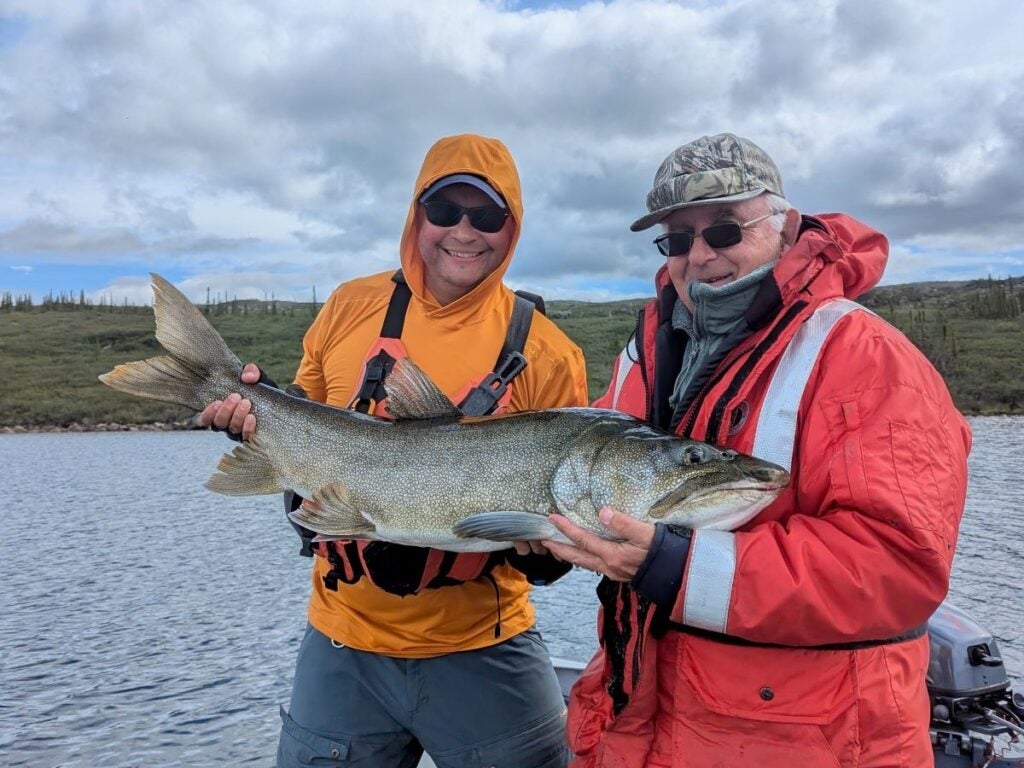 Two men smiling holding a large lake trout on a summer day