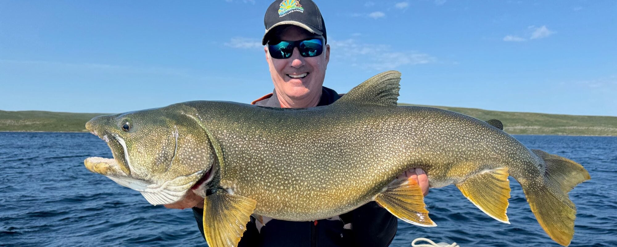 Man holding a huge lake trout on a beautiful summer day