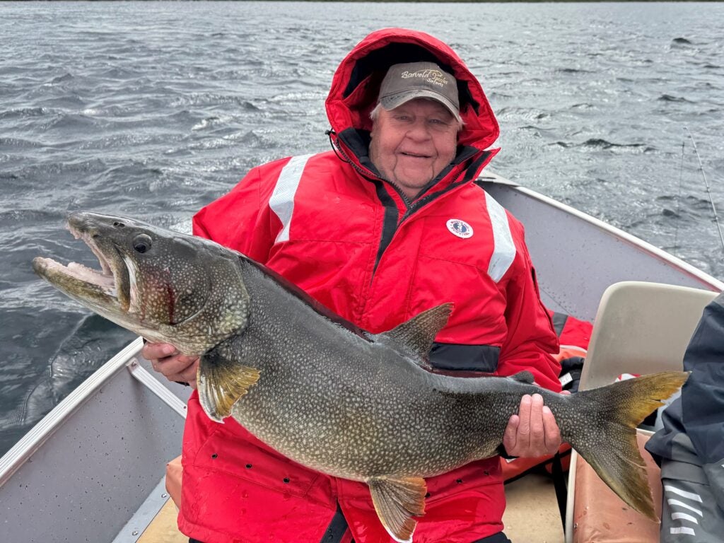 Man wearing a red Mustang floater jacket holding a huge lake trout