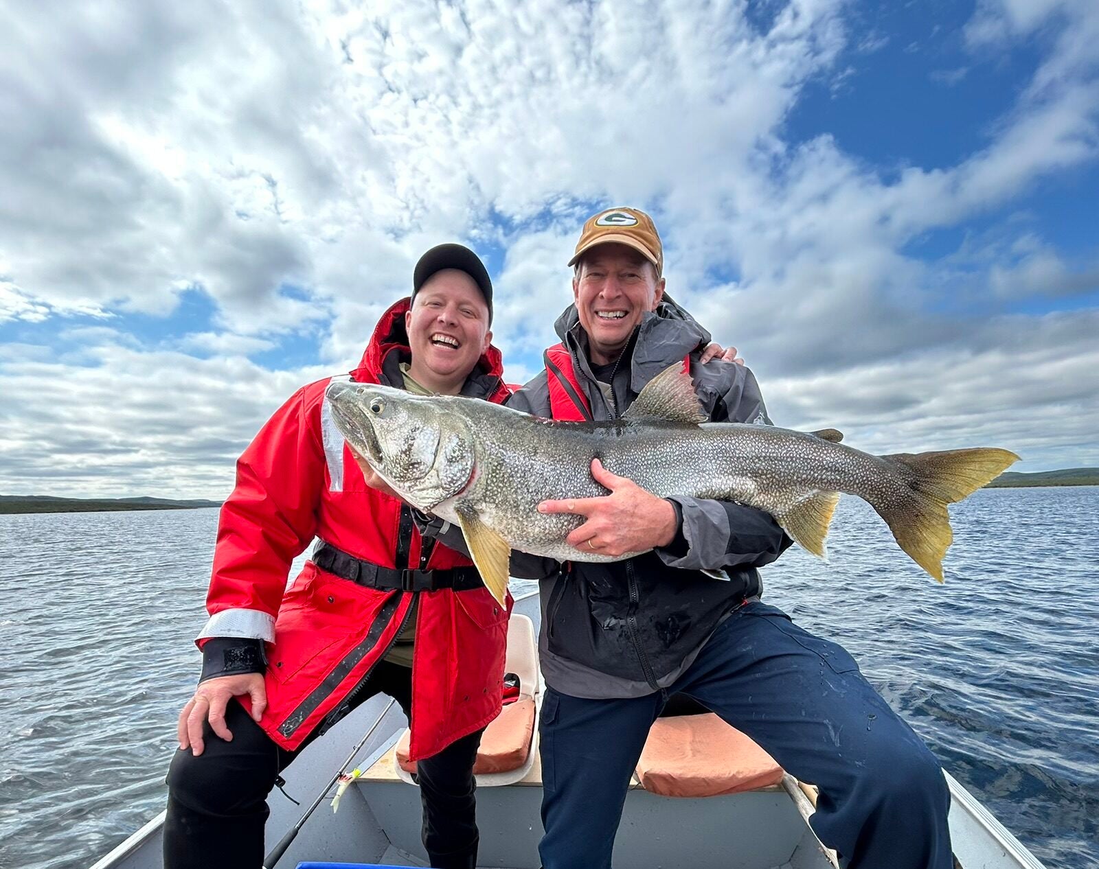 Father and son holding a trophy lake trout on a boat during a fly-in lake trout fishing trip in Canada.