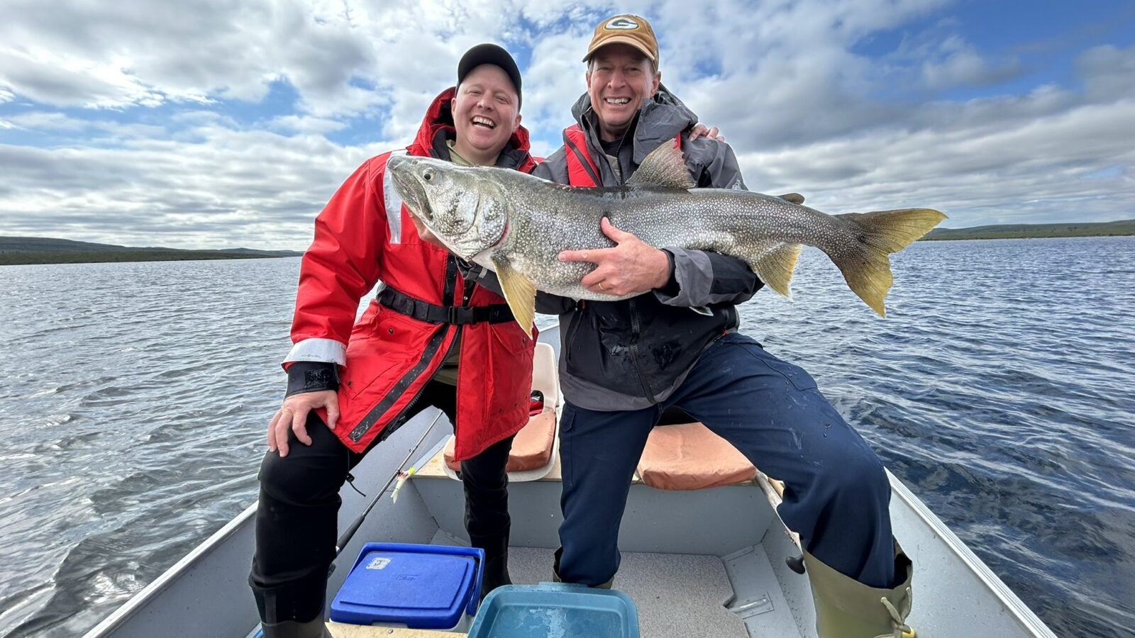 Father and son holding a trophy lake trout on a boat during a fly-in lake trout fishing trip in Canada.